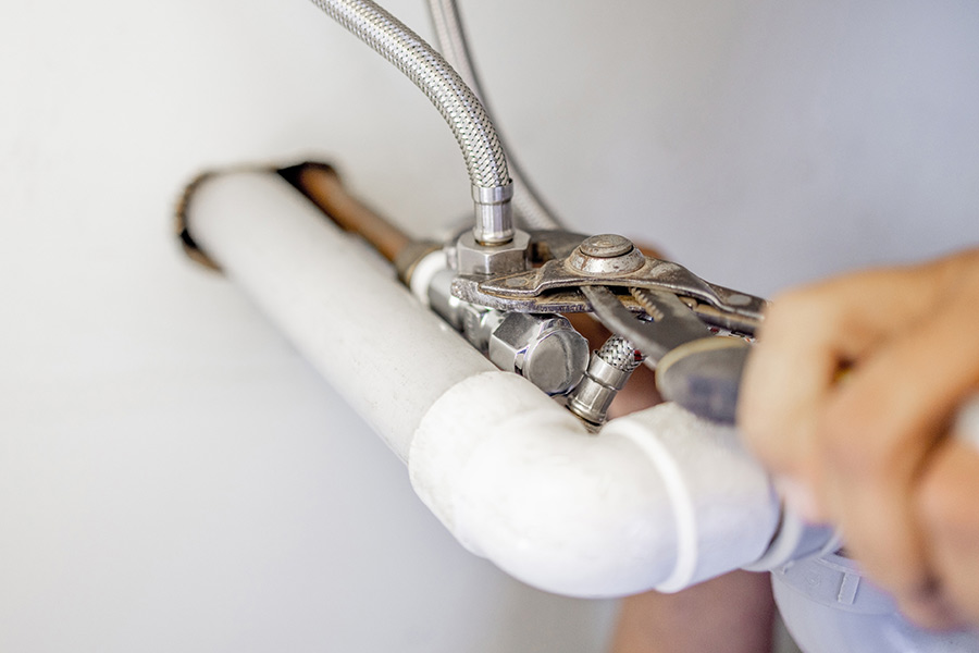Plumber using pliers to tighten a pipe connection.
